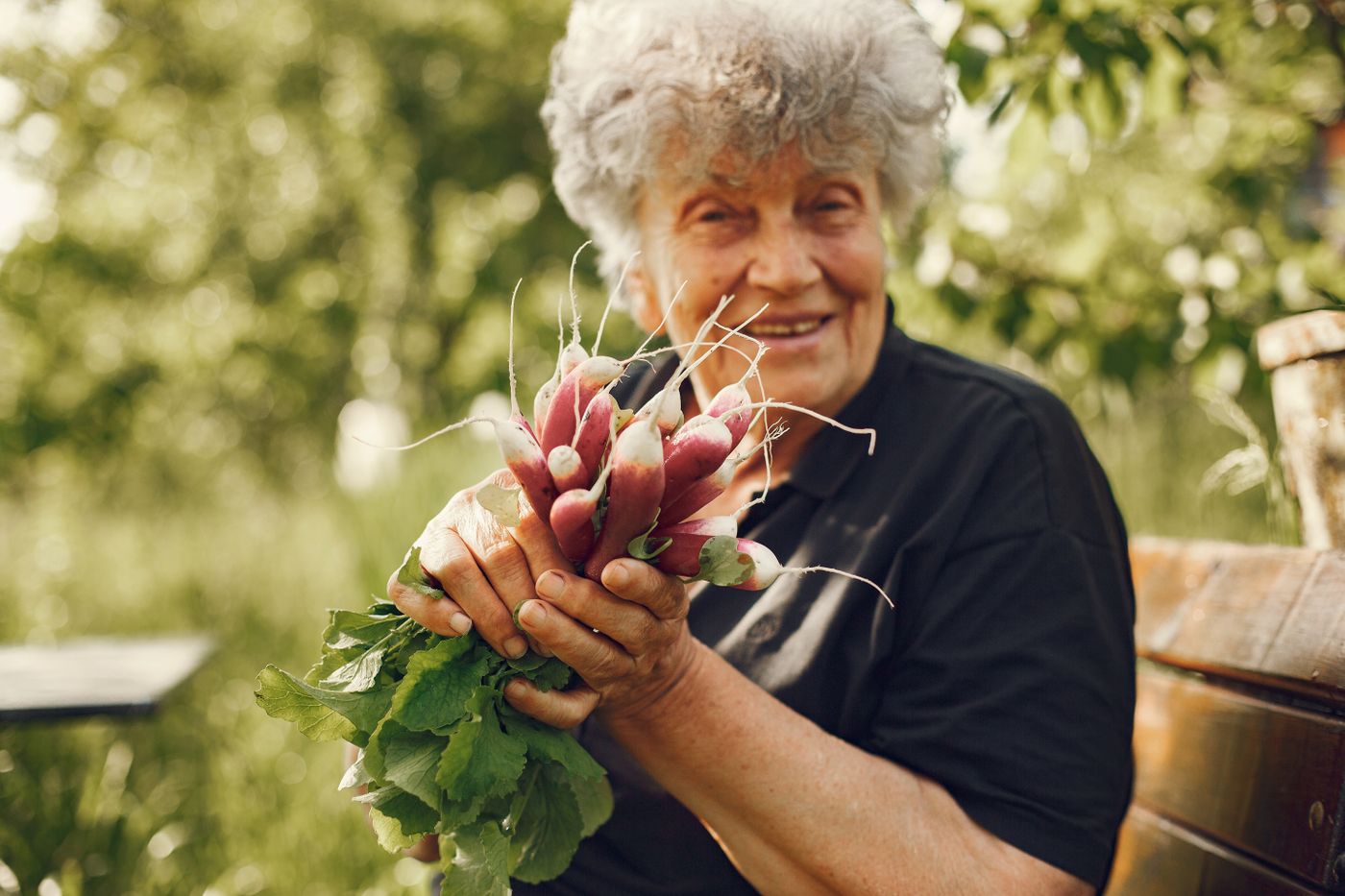 A smiling woman holding freshly harvested vegetables from her garden